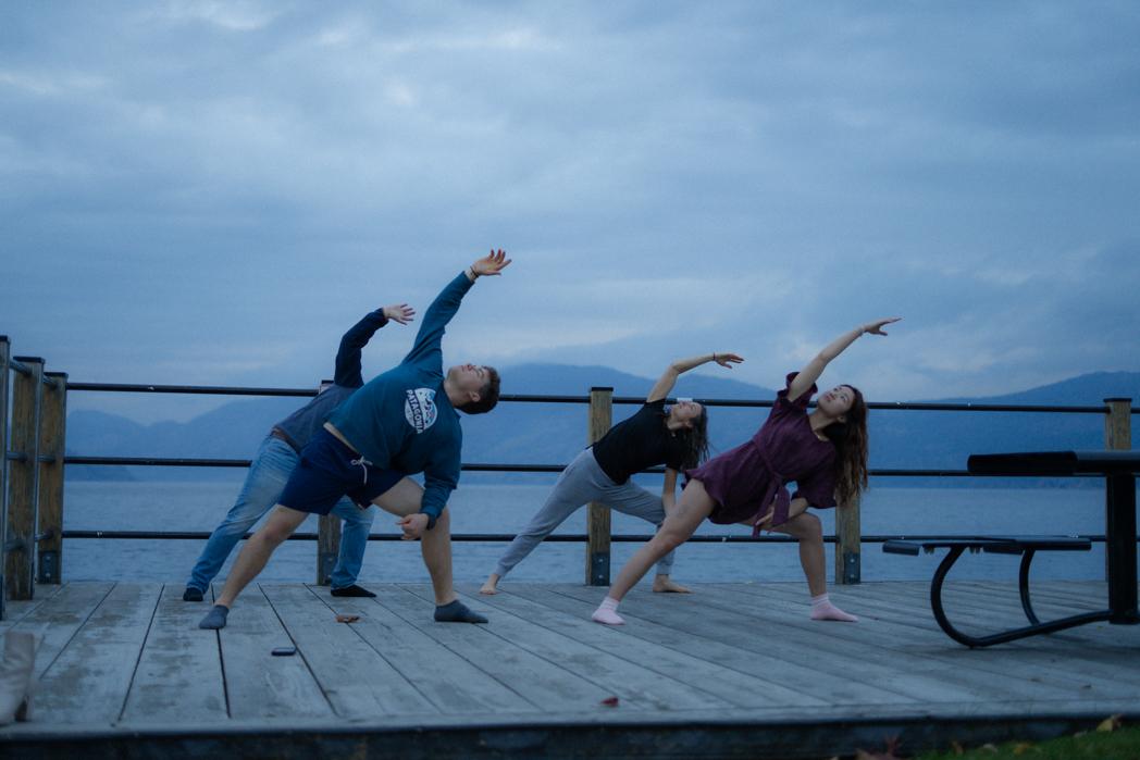 Three guests doing barre stretches on the Peachland dock at dusk with Okanagan Lake and the mountains behind them, a Sweat Culture wellness session