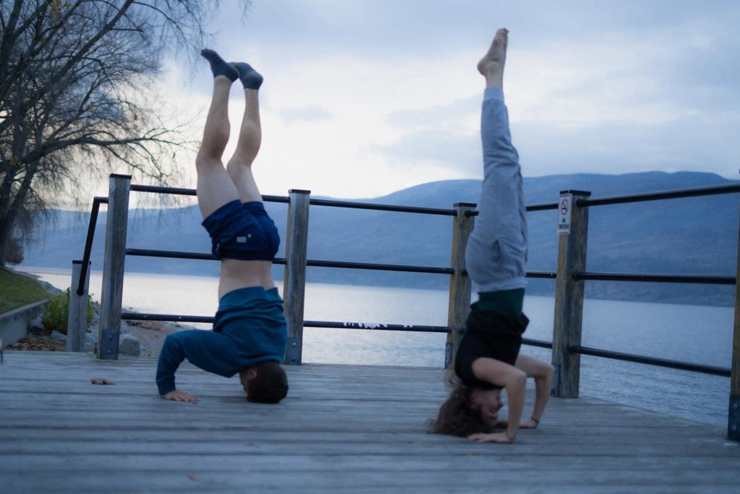 Two guests doing handstands on the dock overlooking Okanagan Lake in Peachland after a Sweat Culture sauna and cold plunge session