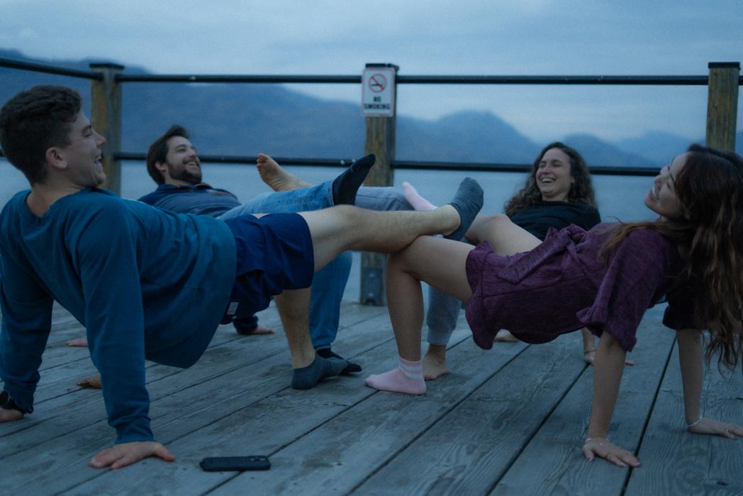 Group of guests laughing while doing leg raises on the dock at Peachland Beach, fun and community at a Sweat Culture sauna session, Okanagan BC