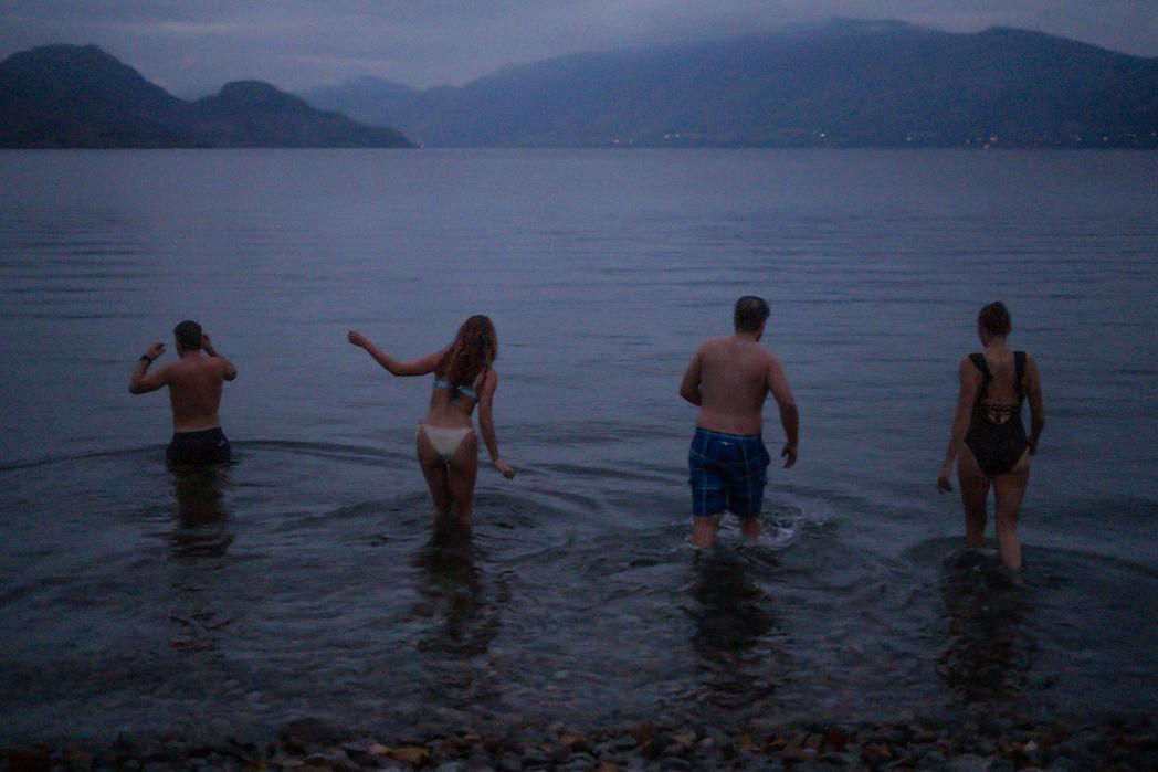 Four guests wading into Okanagan Lake for a cold plunge at dusk after a wood-fired sauna session at Sweat Culture in Peachland, BC