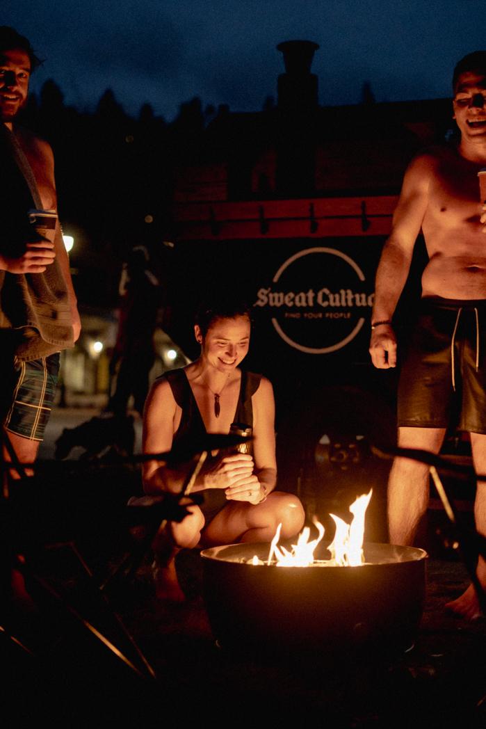 Friends gathered around the fire pit outside the Sweat Culture sauna at night, a community wellness session on Peachland Beach, Okanagan BC