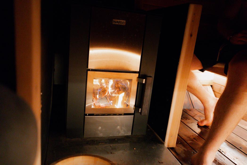 Narvi wood-fired sauna stove burning behind glass inside the Sweat Culture trailer sauna, authentic wood fire heat in Peachland