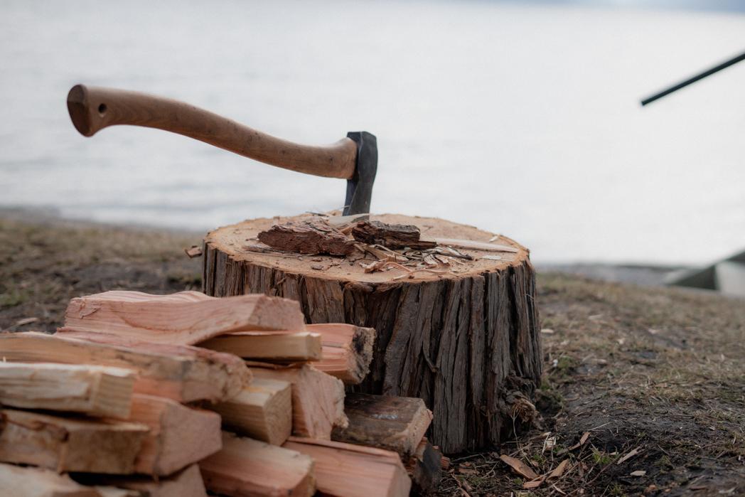 Axe embedded in a wood splitting stump with fresh firewood beside Okanagan Lake, splitting wood for the Sweat Culture wood-fired sauna in Peachland
