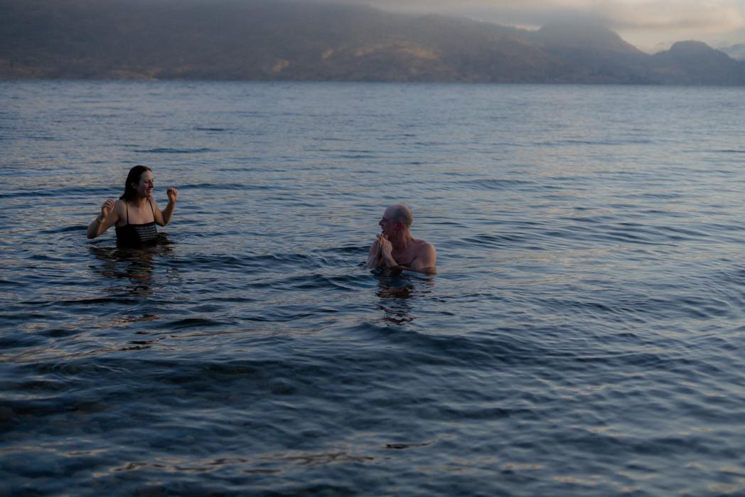 Couple laughing together while cold plunging in Okanagan Lake at sunset, contrast therapy after a Sweat Culture wood-fired sauna session in Peachland, BC