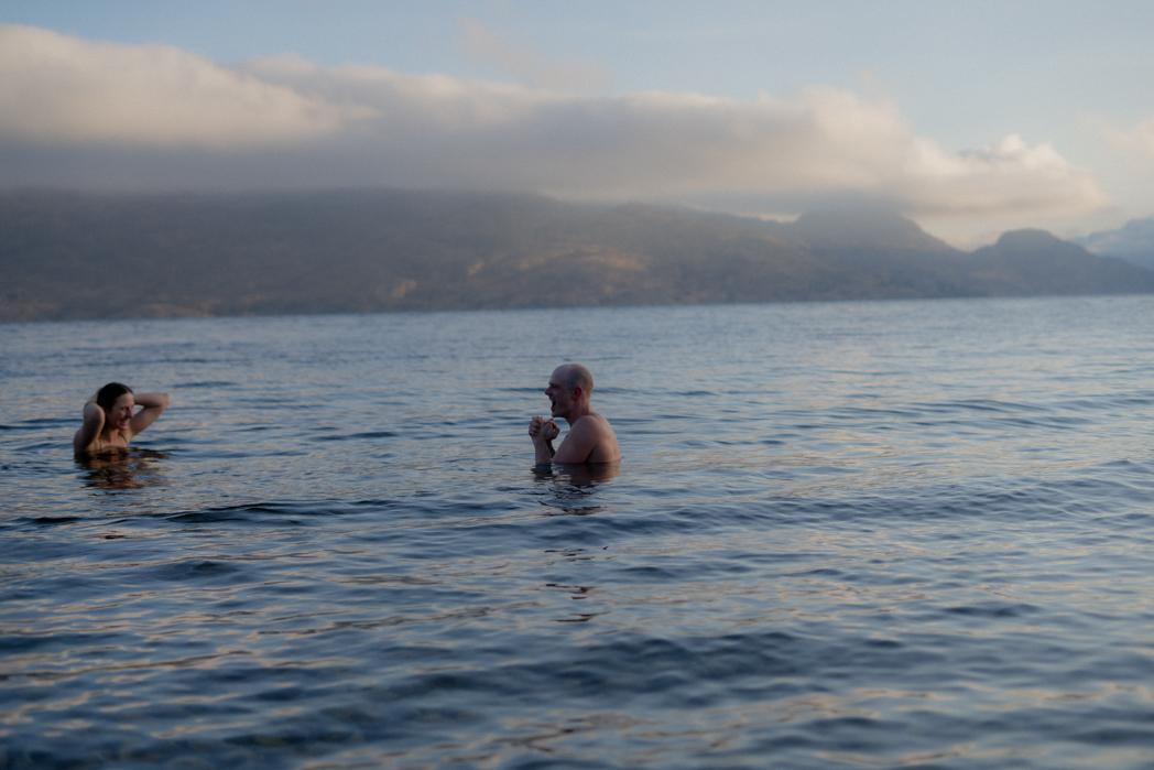 Couple cold plunging together in Okanagan Lake at golden hour, contrast therapy after a Sweat Culture wood-fired sauna session in Peachland, BC